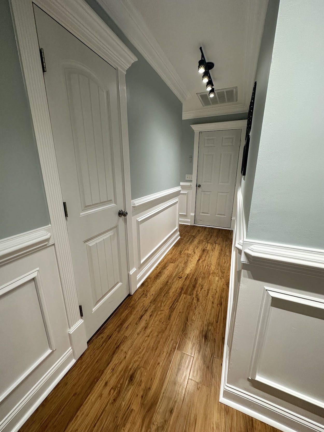 Hallway with warm wood-look vinyl plank flooring and white wainscoting