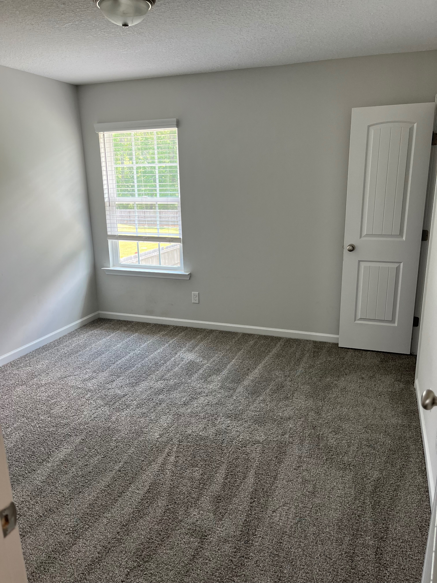 Gray carpet installed in a bedroom with white baseboards and a window